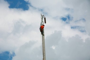 Mavi gökyüzü arka planına sahip elektrik direğinde inşaat işçisi.
