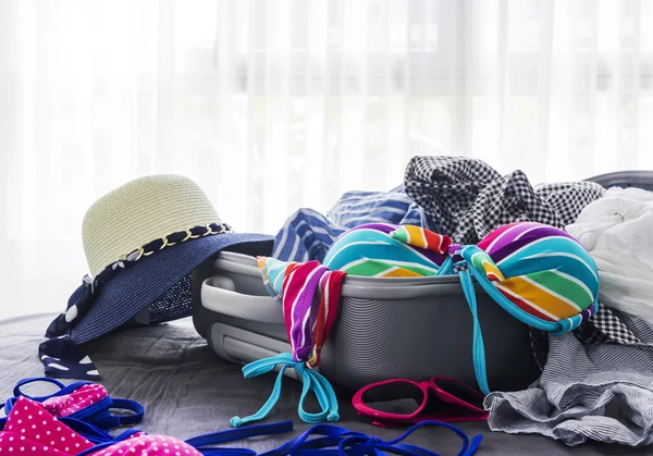 Kolorowe bikini i ubrania w bagażu na łóżku — Zdjęcie stockowe