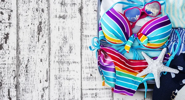 Biquíni colorido e roupas em bagagem no fundo de madeira — Fotografia de Stock