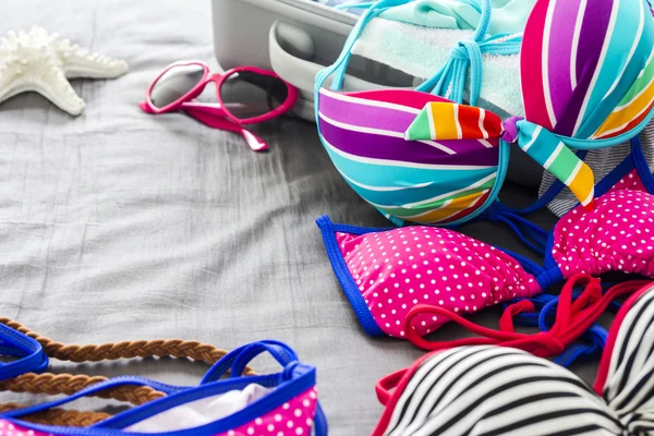 Bikini's en kleding in bagage op het bed — Stockfoto