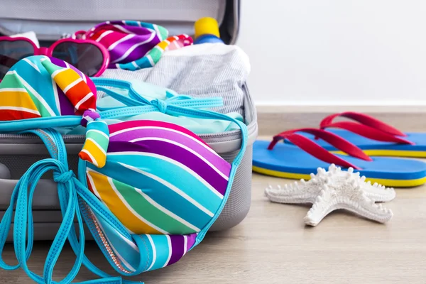 Biquíni colorido e roupas na bagagem no piso laminado — Fotografia de Stock