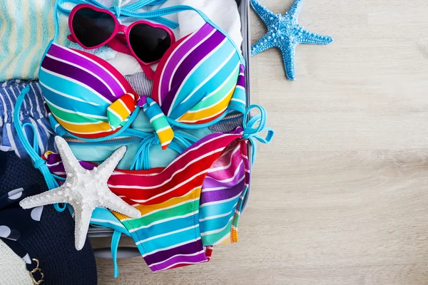 Biquíni colorido e roupas na bagagem no piso laminado — Fotografia de Stock