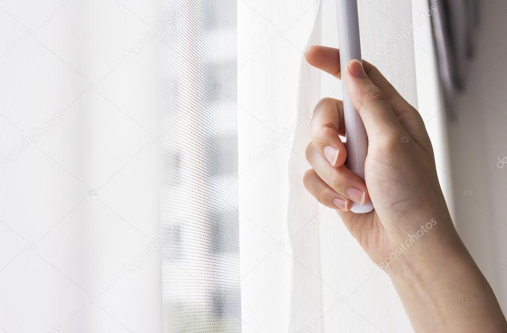 Young woman opening curtains in bedroom