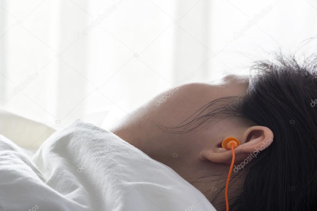 Young woman with earplugs sleeping on the bed