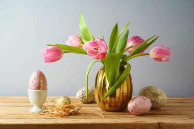 Paskalya tatili konsepti. Güzel lale çiçekleri, ahşap masa üzerinde pembe ve altın yumurtalar.