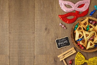 Ahşap tabakta hamantaschen kurabiyeleri ve masa arkasında karnaval maskesi olan Yahudi bayramı Purim konsepti