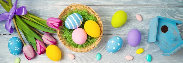 バスケットにイースターの卵と木の背景にチューリップの花とイースターの休日の概念 — ストック写真