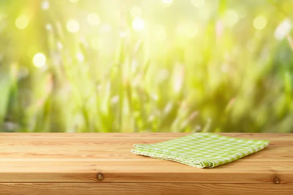 緑の芝生の上にテーブルクロスと空の木製のテーブルの背景がぼやけている 春とイースターモックアップのためのデザイン — ストック写真