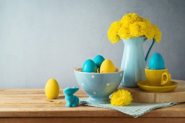 Paskalya bayramı konsepti Paskalya yumurtaları, çiçekler ve ahşap masa üzerindeki tavşan süslemeleri.