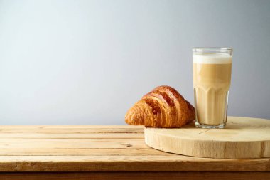 Kahve fincanı ve kruvasan gri arka plandaki ahşap masada.
