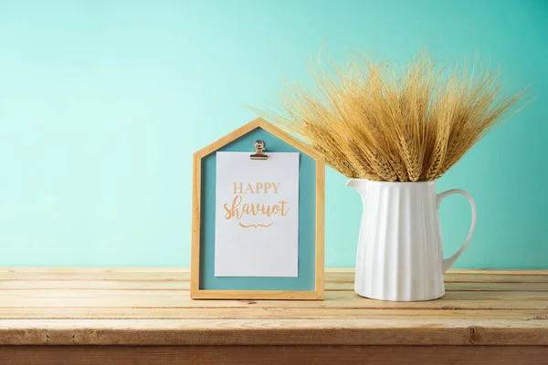青い壁の背景に木製のテーブルの上の花瓶や写真フレームに小麦 Shavuot休日モックアップのためのデザイン — ストック写真