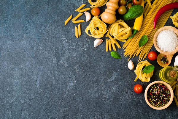 Italian pasta, tomatoes, basil herbs and spices over dark background. Italian cuisine concept