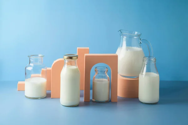 Milk bottles and milk jug over blue background. Modern still life composition. Healthy eating concept