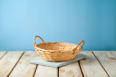 Mavi duvar arkaplanının üzerinde masa örtüsü olan boş bir hasır sepet. Mutfak tasarım ve ürün gösterimi için hazırlandı.