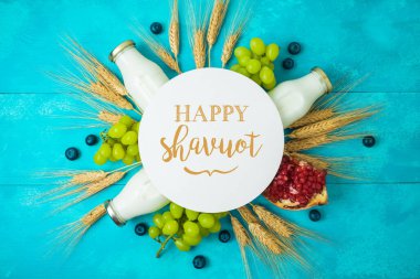 Yahudi bayramı Shavuot tebrik kartı. Süt şişesi, buğday kulağı ve ahşap masa arkasında üzümler.