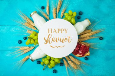 Jewish holiday Shavuot greeting card with milk bottle, wheat ears and grapes on wooden blue table background clipart