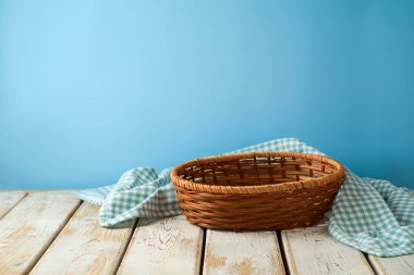 Mavi duvar arkaplanının üzerinde tahta masa örtüsü olan boş bir sepet. Mutfak tasarım ve ürün gösterimi için hazırlandı.
