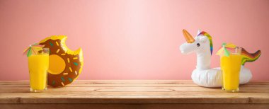 Portakal suyu ve parti havuzu olan tropikal yaz tatili konsepti pembe arka planda ahşap masada yüzüyor.