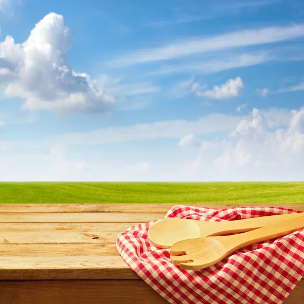 Wooden table with kitchen utensil over green meadow and blue sky — Stock Photo, Image