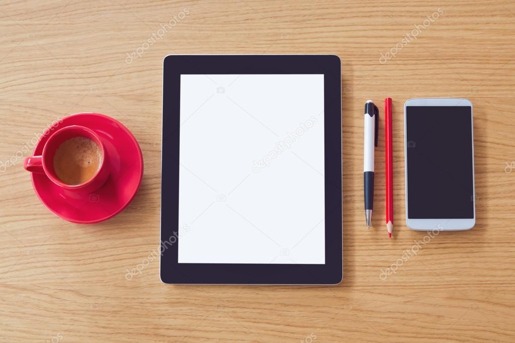 Tablet with blank screen and smartphone with cup of coffee on wooden table. Office desk mock up. View from above