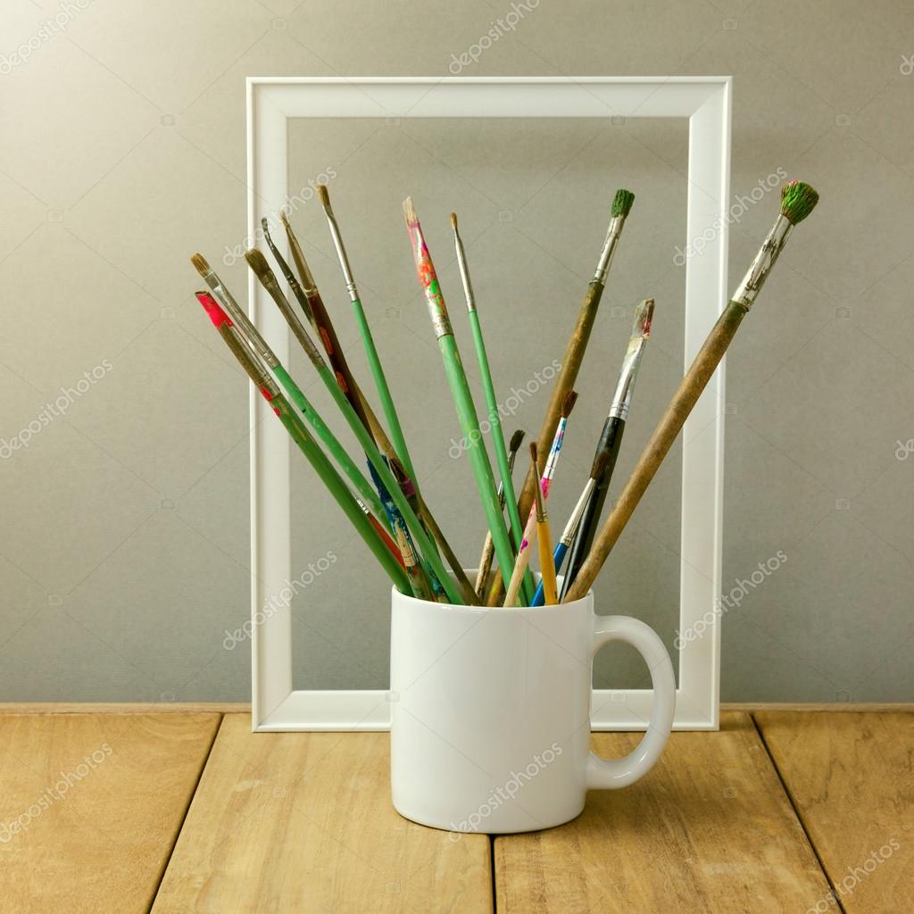 Painter brushes in white cup on wooden table. Cup for logo display mock up
