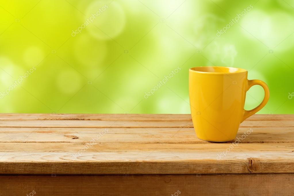 Yellow cup on wooden table over green bokeh background