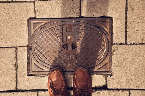 Sewer manhole with feet in shoes — Stock Photo, Image