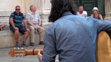 VENICE - 24 Temmuz 2018: Duvarda dinlenen turistlerin önünde gitar çalan bir sokak müzisyeninin yakın çekimi.