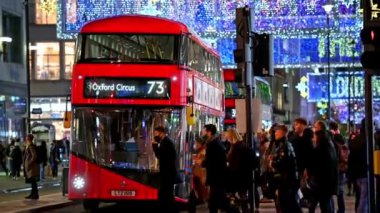 NOVEMBER 3, 2020: Oxford Caddesi 'nin aydınlatılmış Noel süslemelerini göstermek için Noel alışverişçileri ve kırmızı Londra çift katlı otobüslerden yana eğilin