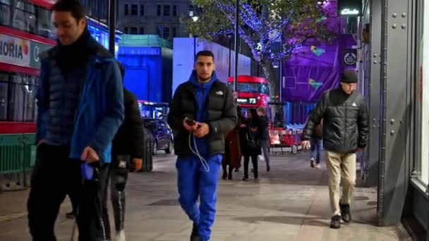 ロンドン 2020年11月3日 買い物客は夜にオックスフォード ストリートの歩道を歩いて 背景に赤いロンドン ダブル デッカー バスを含む交通量で歩きます — ストック動画