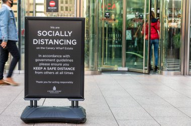 Londra - 4 Kasım 2020: Kanarya Rıhtımı 'ndaki bir binanın önünde, arka planda dönen kapılar olan 19 sosyal uzaklık tabelası