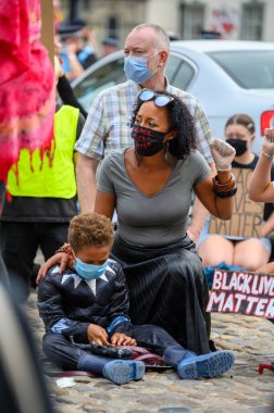 Richmond, Kuzey Yorkshire, İngiltere - 14 Haziran 2020: Güçlü BAME kadını BLM protestosunda oğlunu tutarken Siyah Yaşamlar Önemli PPE Yüz Maskesi takıyor ve selam veriyor
