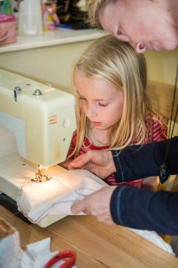 Küçük kızına dikiş makinesi kullanmayı öğreten bir annenin yakınına..