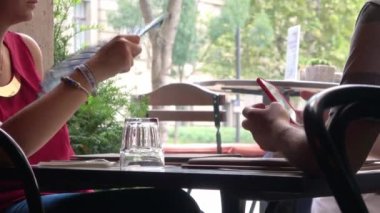 BUDAPEST - 21 Ağustos 2018: Ortağı Budapeşte, Macaristan 'da bir açık kafede cep telefonu kullanırken, bir kadının serinlemek için kendini yelpazelemesi