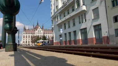 BUDAPEST - 21 AĞUSTOS 2018: Macaristan 'ın Budapeşte şehrinde güneşli bir günde arka planda Macar Parlamento Binası ile Tramvaylar alçak açılı çekim.