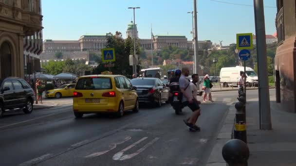 BUDAPEST - AUGUST 21, 2018: Gyalogosok átkelnek a forgalmas budapesti úton egy napsütéses napon a Budapesti Várral a háttérben.
