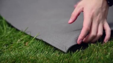 KADIN ellerinin çimden yoga minderini kaldırdığı sığ odak görüntüsünü kapatın..