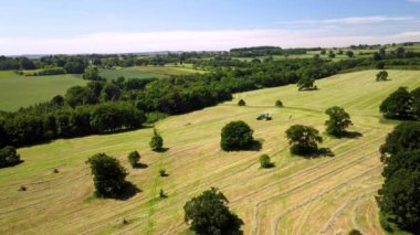 Yüksek irtifa, geniş açılı hava aracı görüntüsü. Bir traktörün karavan çekişi. Bir tahıl biçme makinesinin yanında.