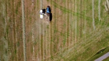 Yüksek irtifada havada uçan bir traktörün karavan çekerken görüntüsü. Bir tahıl hasatçısının yanında. Ekin için ot kesimi topluyor.