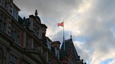 Geleneksel Londra binalarının üzerinde bayrak dalgalanırken, arka planda çarpıcı bir gökyüzü vardı..
