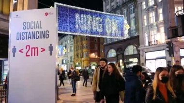 LONDON - 3 Kasım 2020: Covid 19 Sosyal Mesafe tabelası ve Oxford Caddesi gece vakti Noel alışverişçileri ile aydınlatılmış Noel süslemeleri