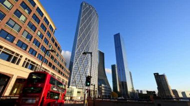 Londra, İngiltere - 4 Kasım 2020: Kırmızı bir Londra Double Decker otobüsü ve Canary Wharf gökdelenlerinin altındaki diğer trafik geçidi batan güneşin altın ışığıyla yıkandı