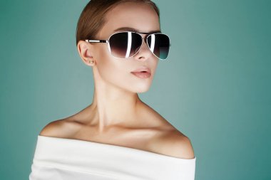 Güneş gözlüklü güzel bir kadın. Yeşil arka planda şık bir bayan.