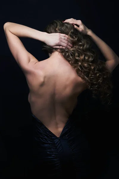 beautiful back of young woman in a black sexy dress.luxury beauty brunette Girl curly healthy hair