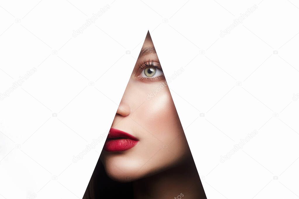 young beautiful woman with a bright makeup. make-up artist concept. A girl with beautiful green eyes, looks into the hole of white paper