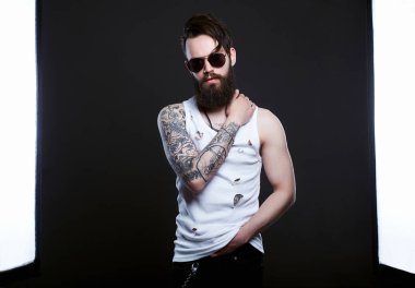 Güneş gözlüklü yakışıklı adam. Gözlüklü, yırtık pırtık gömlekli vahşi sakallı hippi çocuk. sakal, saç kesimi, dövme