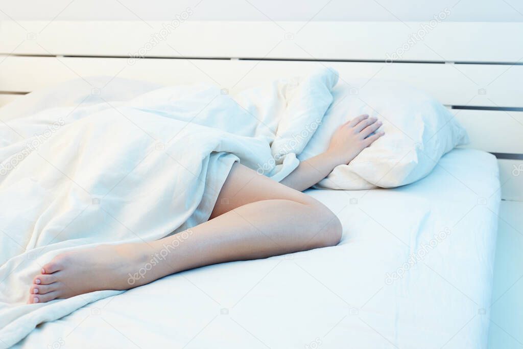 female leg sticking out from under the blanket. Lifestyle photo of girl under the covers on the bed. woman in white morning home