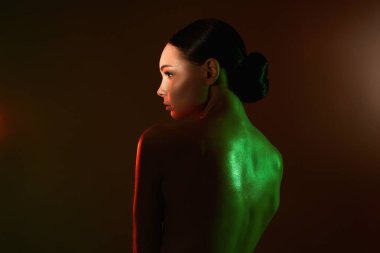 Renkli ışıklar içinde güzel bir genç kadın. Makyajlı ve parlak vücutlu güzel kız.