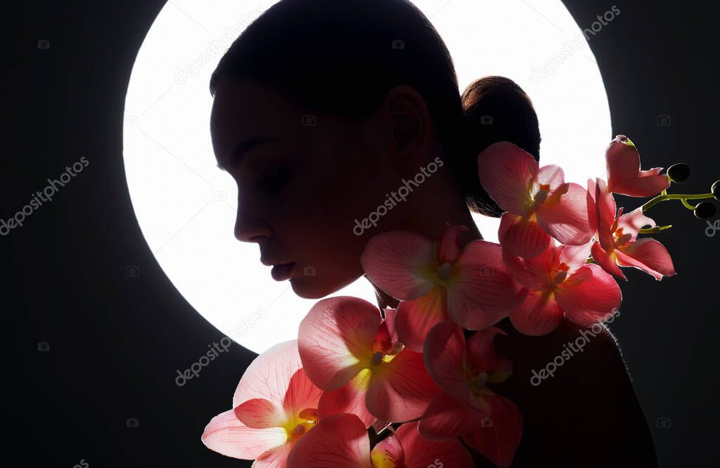 Beautiful young Woman with Orchid flower. female silhouette with flowers on the background of the moon