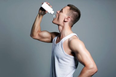 bodybuilder eating pills, steroids. Handsome Fitness Boy with bottle. Sport body muscular Man. Gym